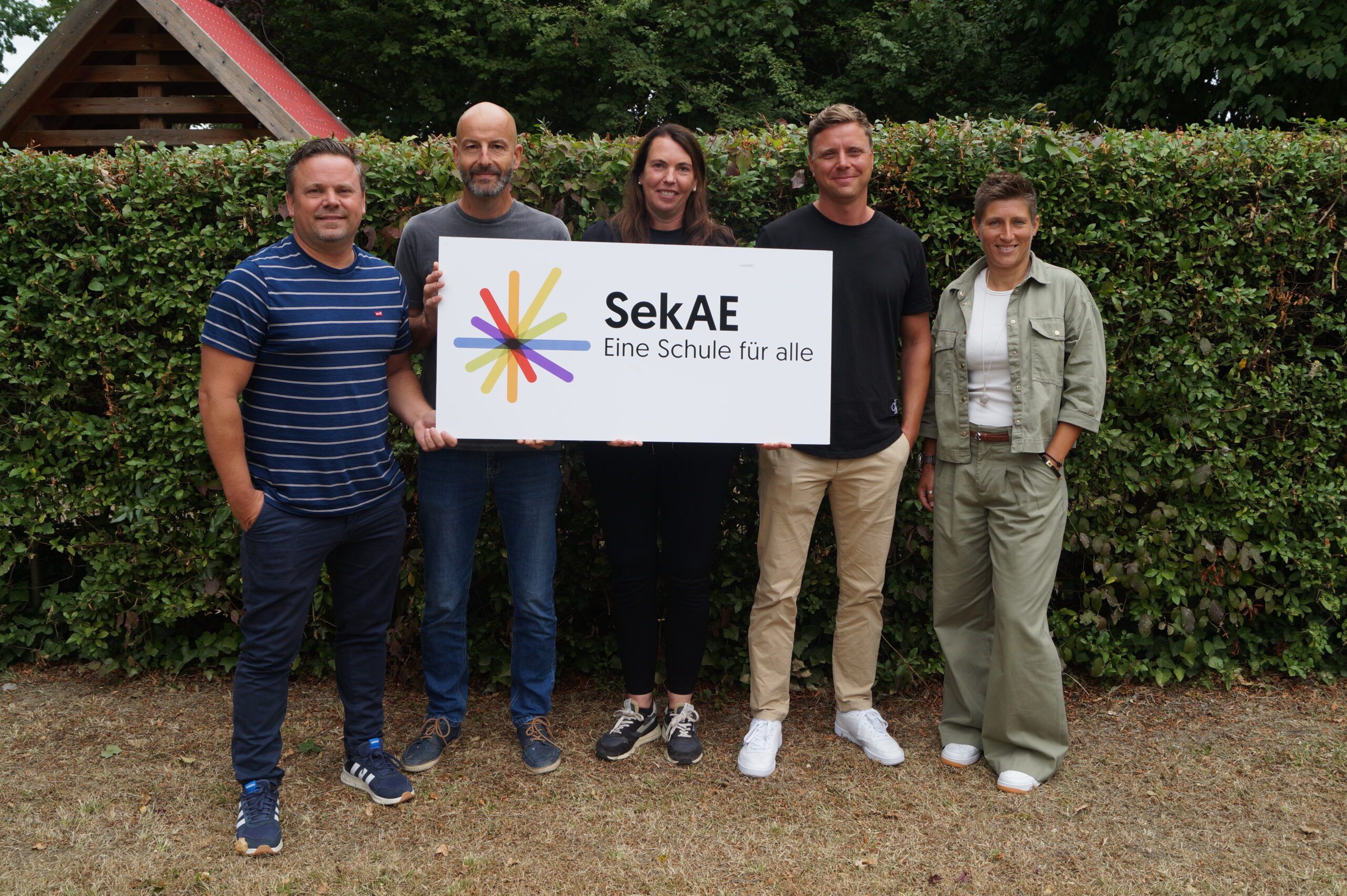 Sechs Personen halten ein Schild mit dem Logo der SekAE