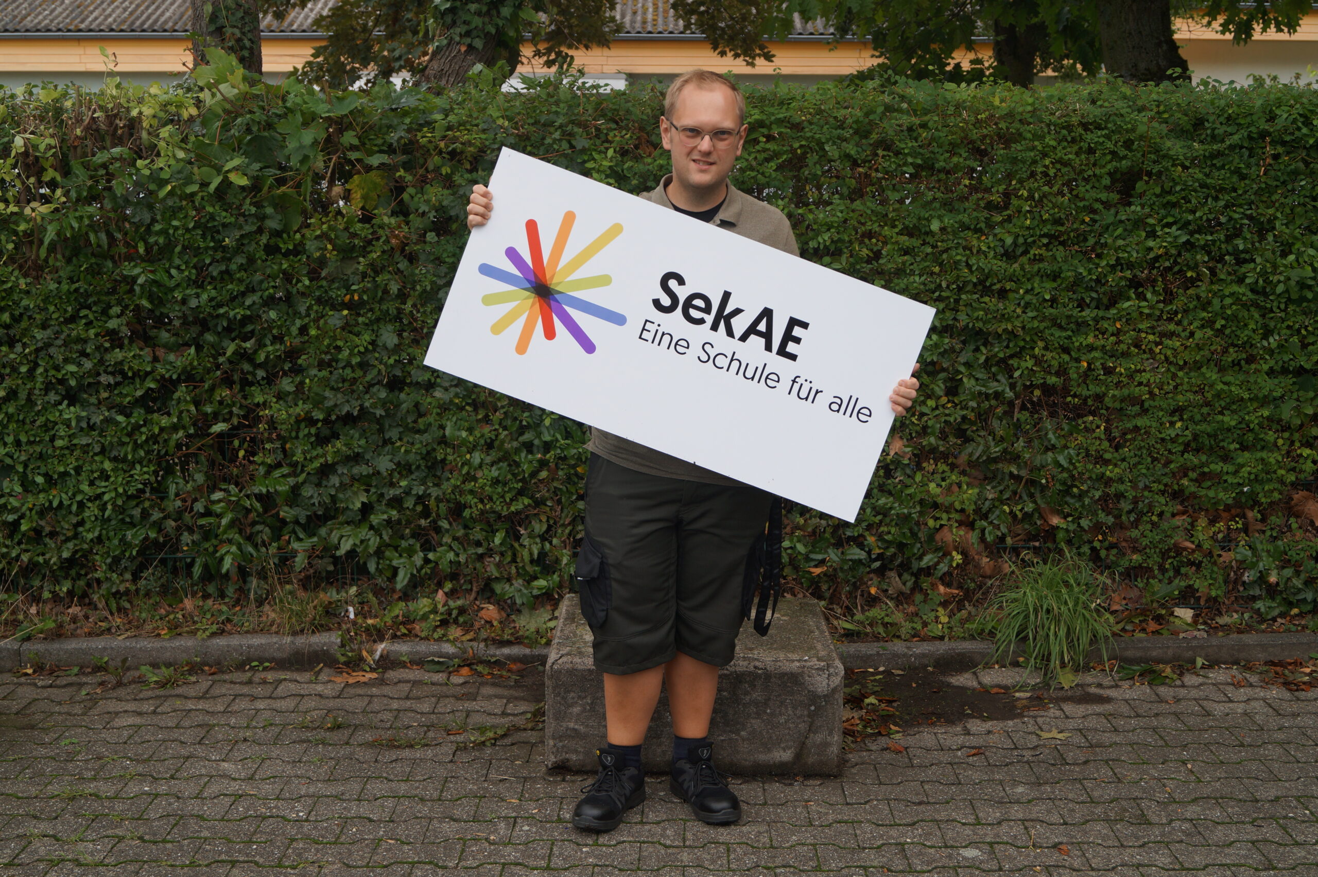 Eine Personen hält ein Schild mit dem Logo der SekAE
