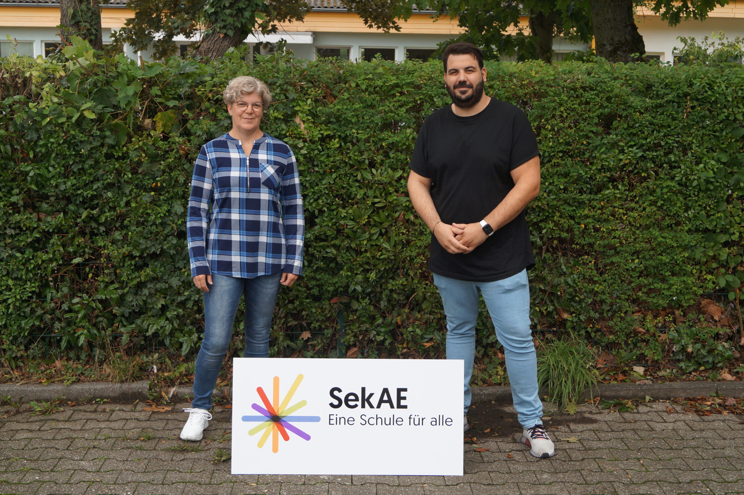 Zwei Personen halten ein Schild mit dem Logo der SekAE