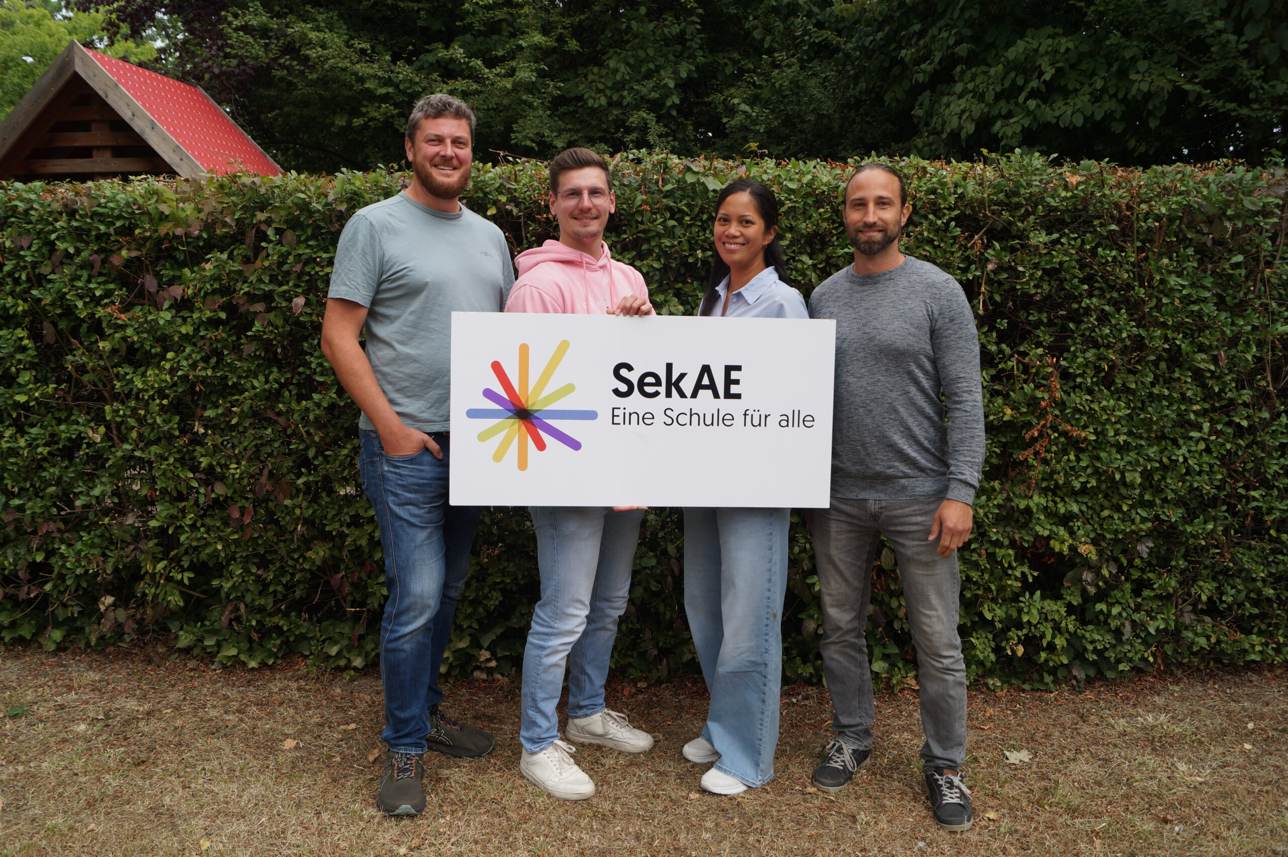 Drei Personen halten ein Schild mit dem Logo der SekAE