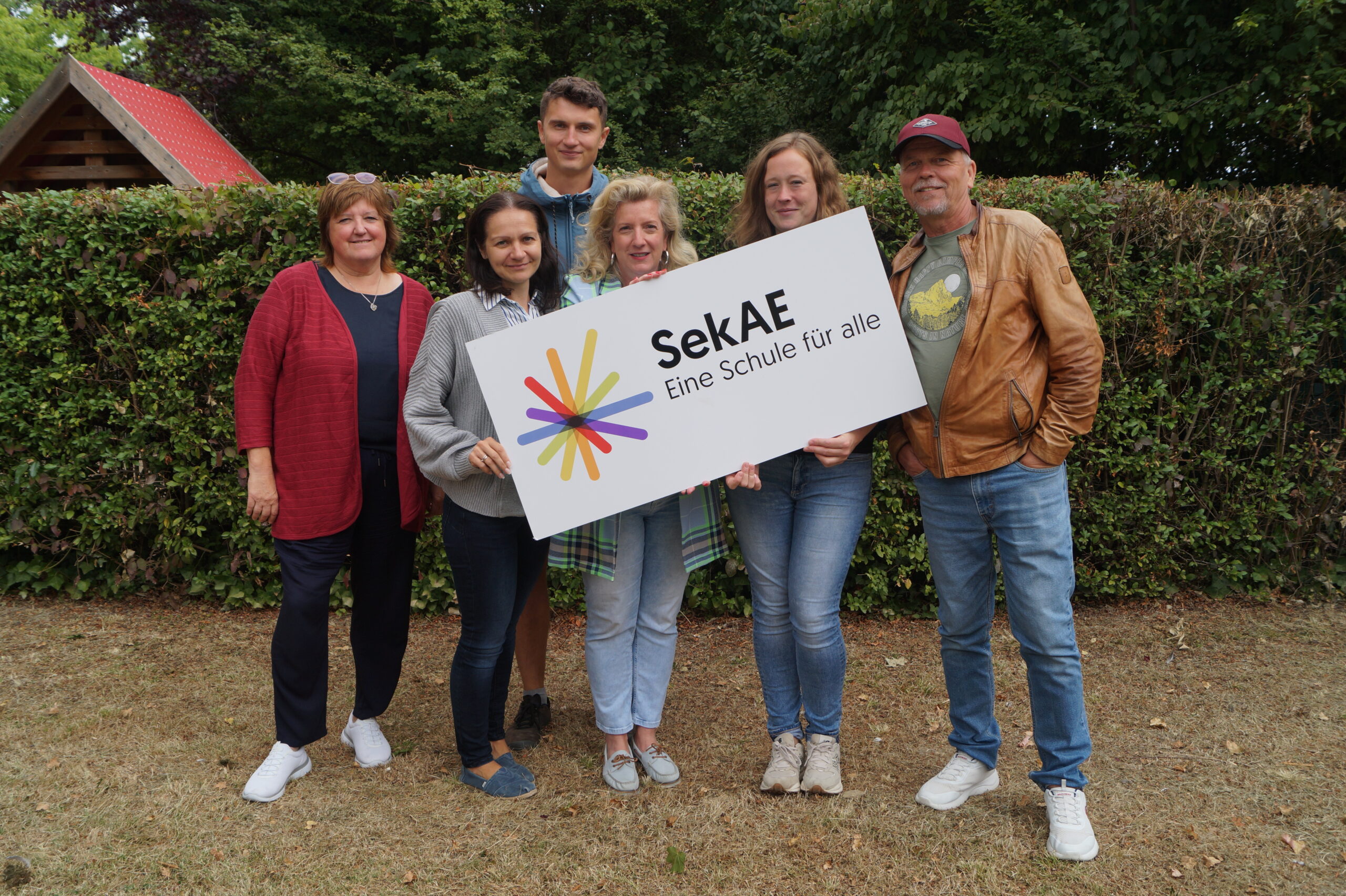 Sechs Personen halten ein Schild mit dem Logo der SekAE