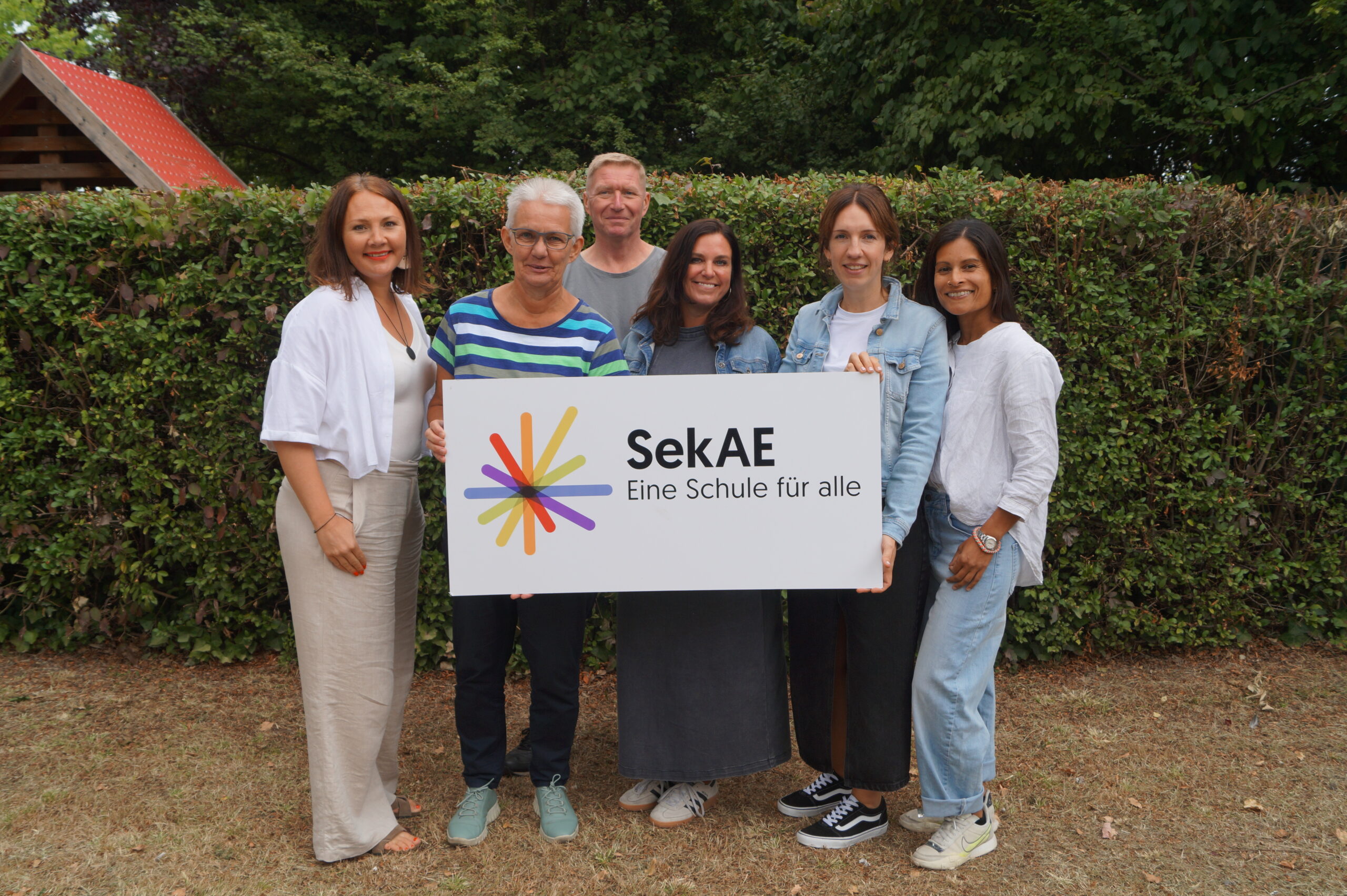 Fünf Personen halten ein Schild mit dem Logo der SekAE