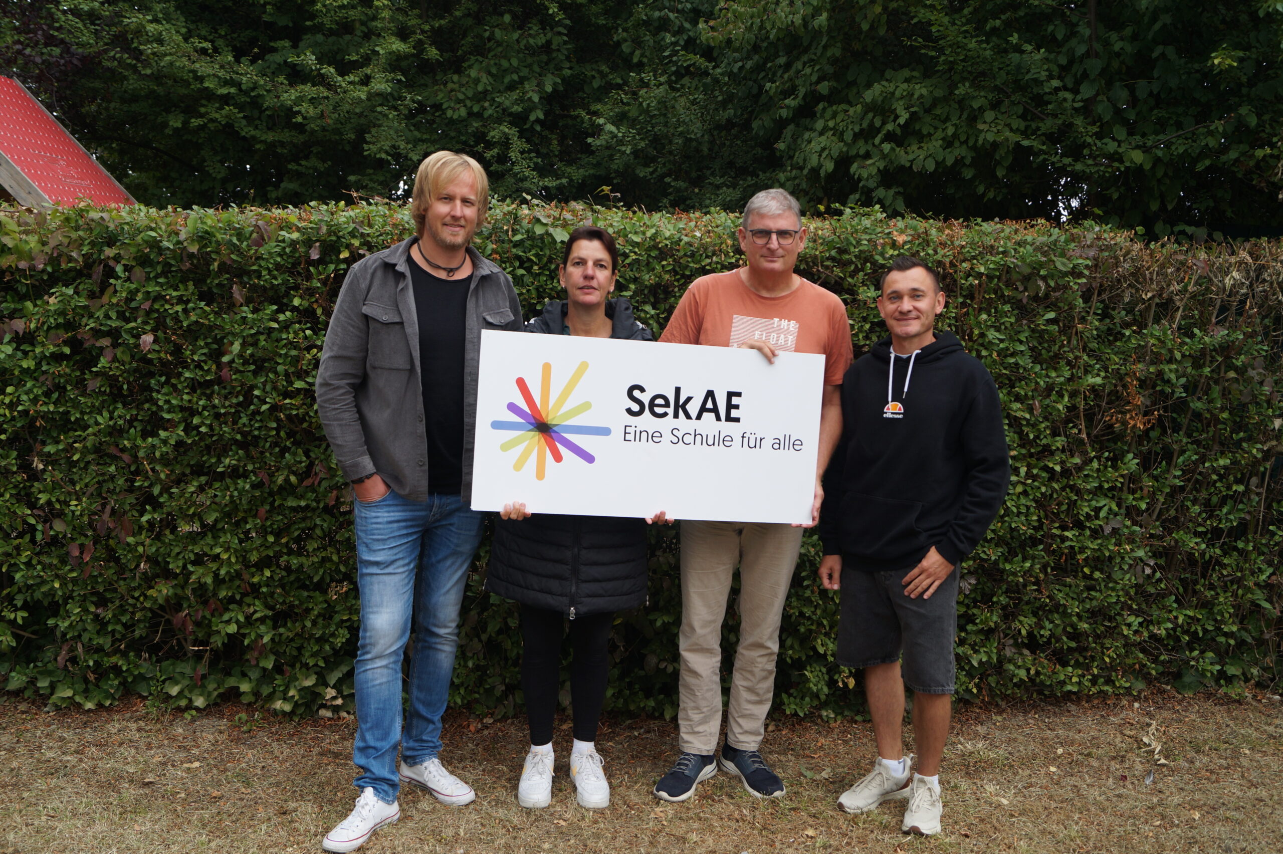 Vier Personen halten ein Schild mit dem Logo der SekAE